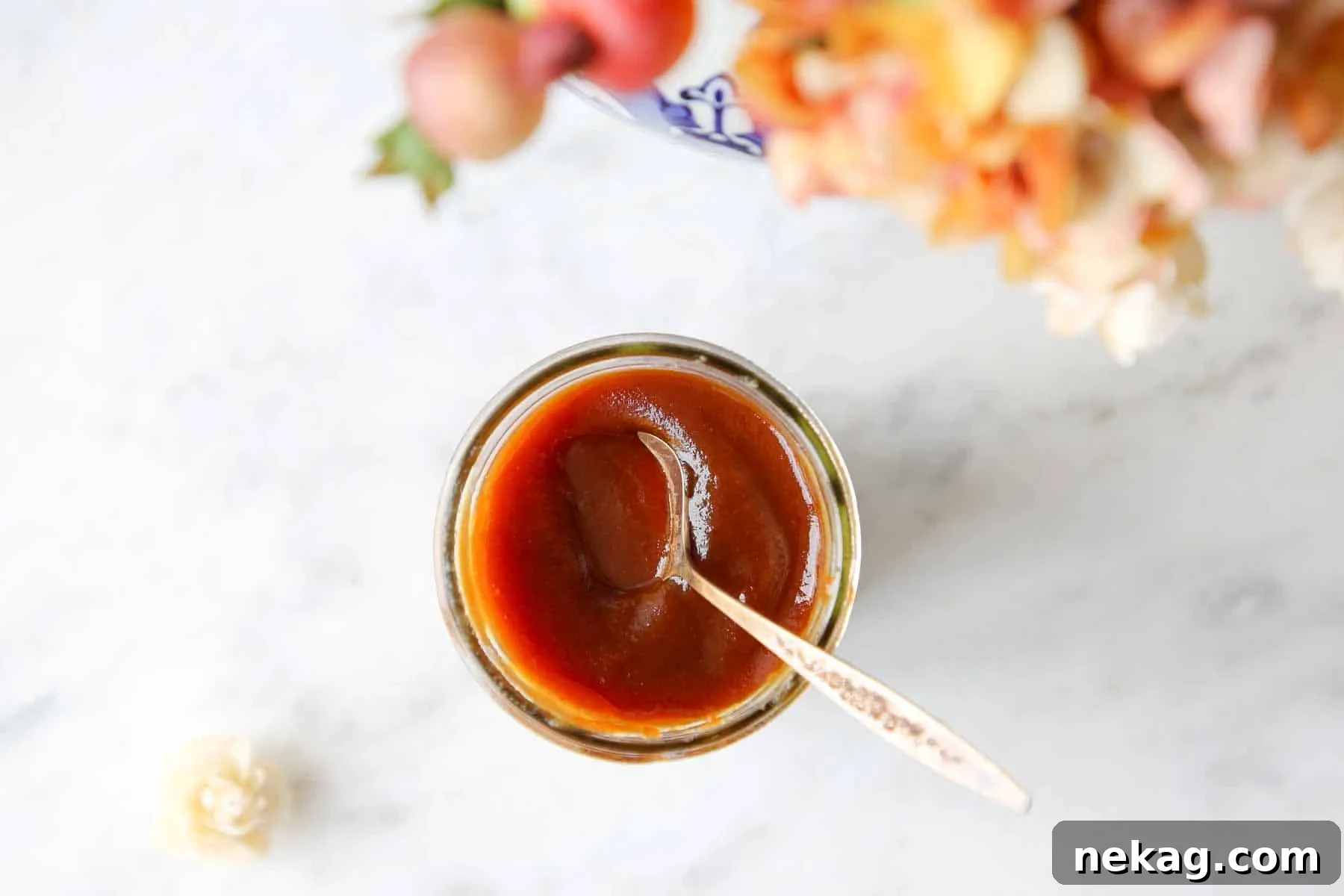 Freshly made apple butter in a jar on a marble countertop, garnished with autumn flowers.