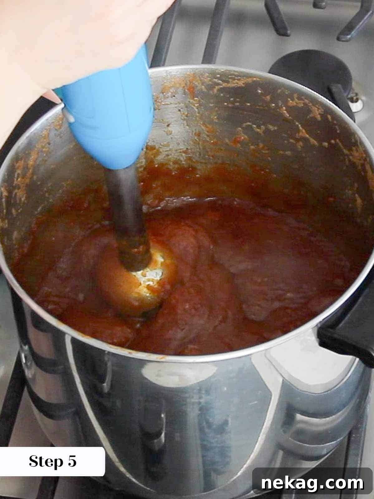 A hand blender immersing into the cooked apple mixture, pureeing it directly in the pot.