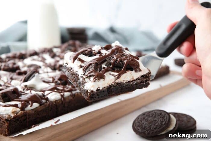 Fudgy Cookies and Cream Brownies 11 A spatula lifting a perfect square of Cookies and Cream Brownie from a pan, showcasing its rich layers of chocolate, marshmallow, and Oreos, ready to be enjoyed.