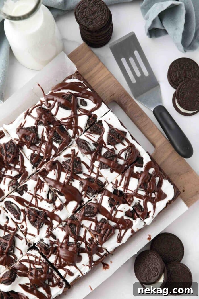 Fudgy Cookies and Cream Brownies 4 A tray of freshly made Cookies and Cream Brownies, beautifully frosted with marshmallow creme, adorned with chopped Oreo cookies, and elegantly drizzled with rich fudge sauce.