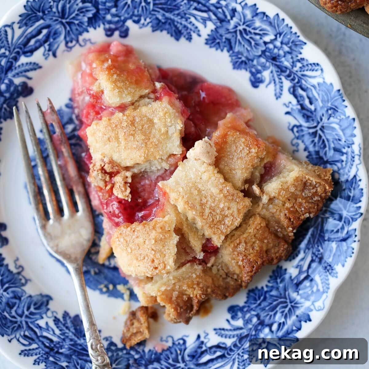 Strawberry Rhubarb Delight 8 A delectable slice of warm Strawberry Rhubarb Pie served on a charming blue plate, perfectly ready to be savored with a dollop of ice cream.