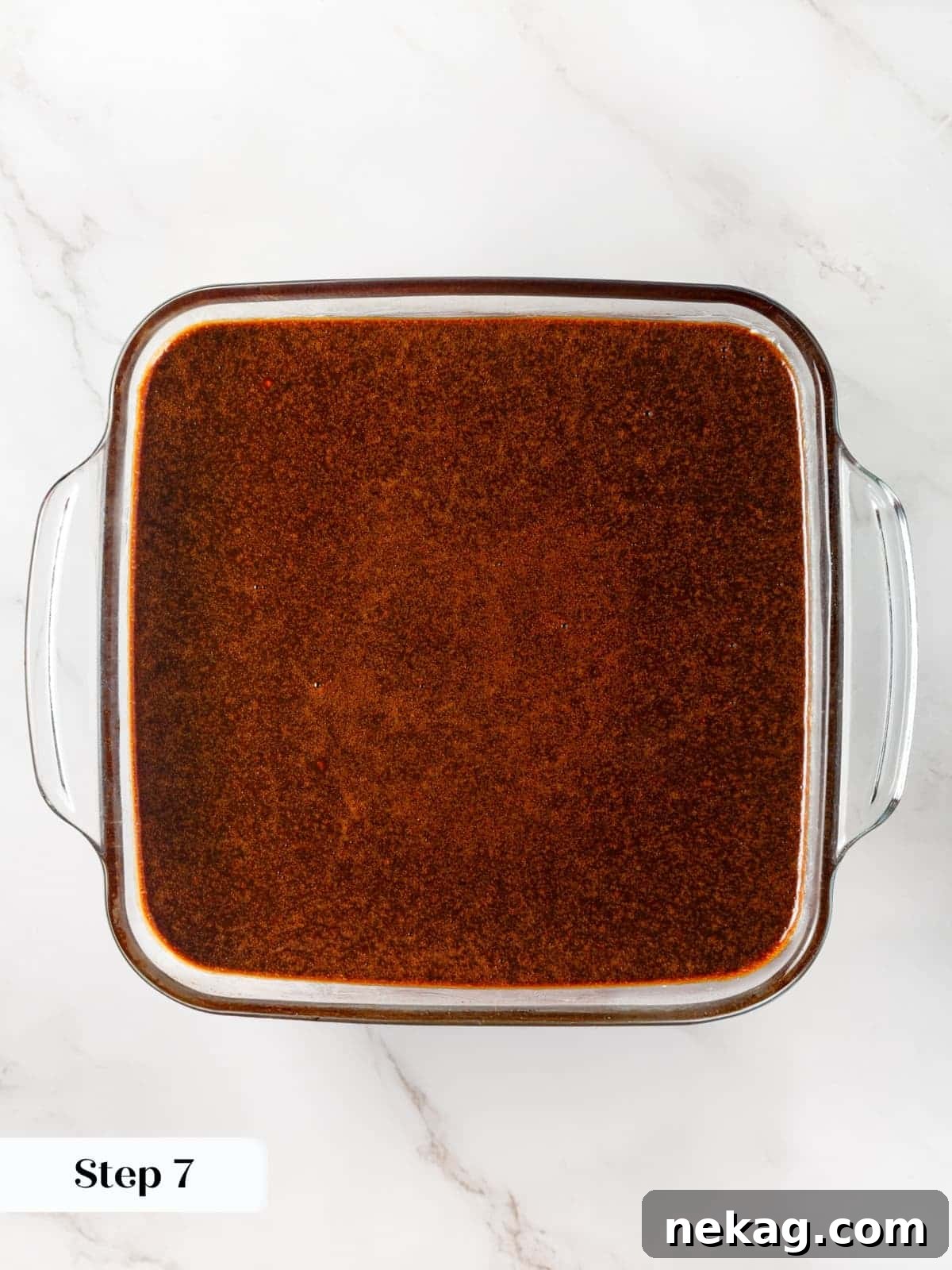 Gingerbread cake batter being poured into a rectangular baking dish lined and prepared.