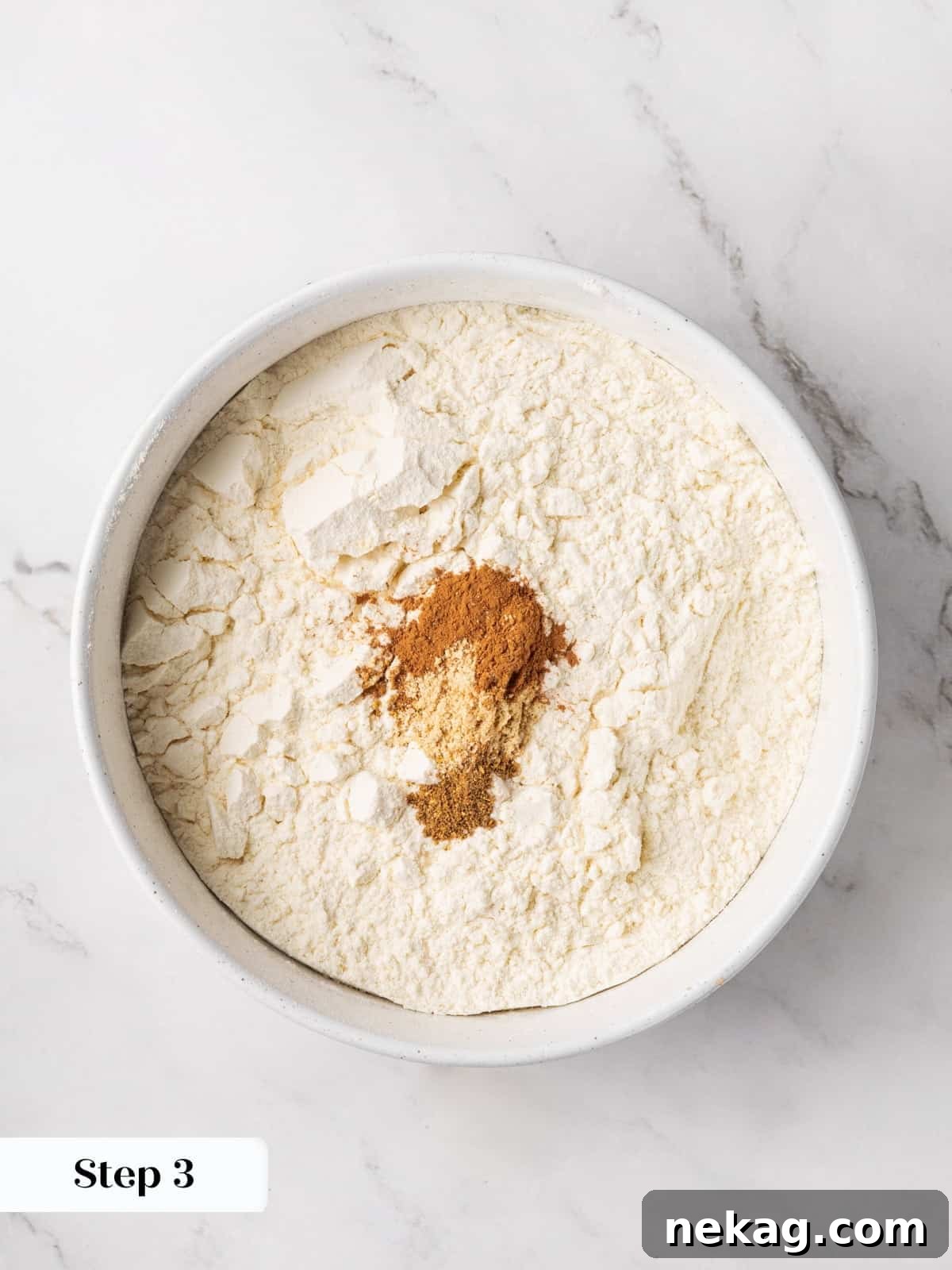 Dry ingredients for gingerbread cake, flour whisked with ginger, cinnamon, and allspice in a bowl.