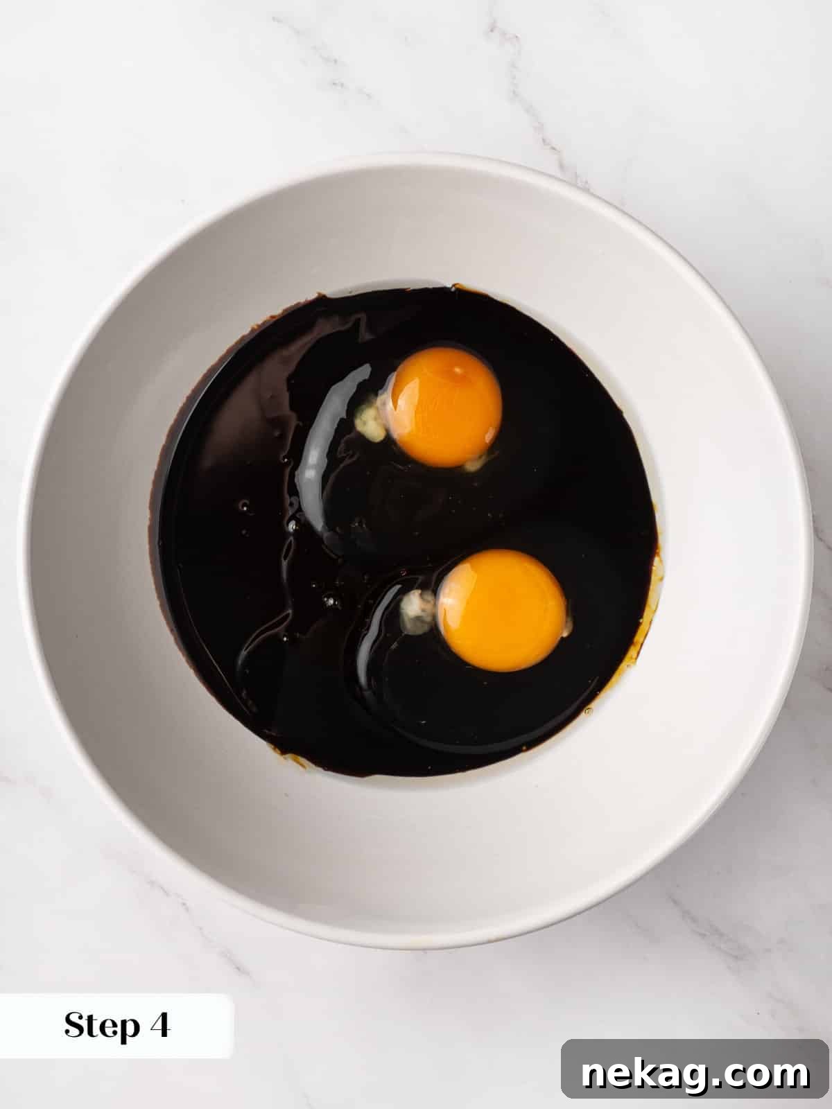 Dark molasses sitting with cracked eggs in a bowl before whisking together.