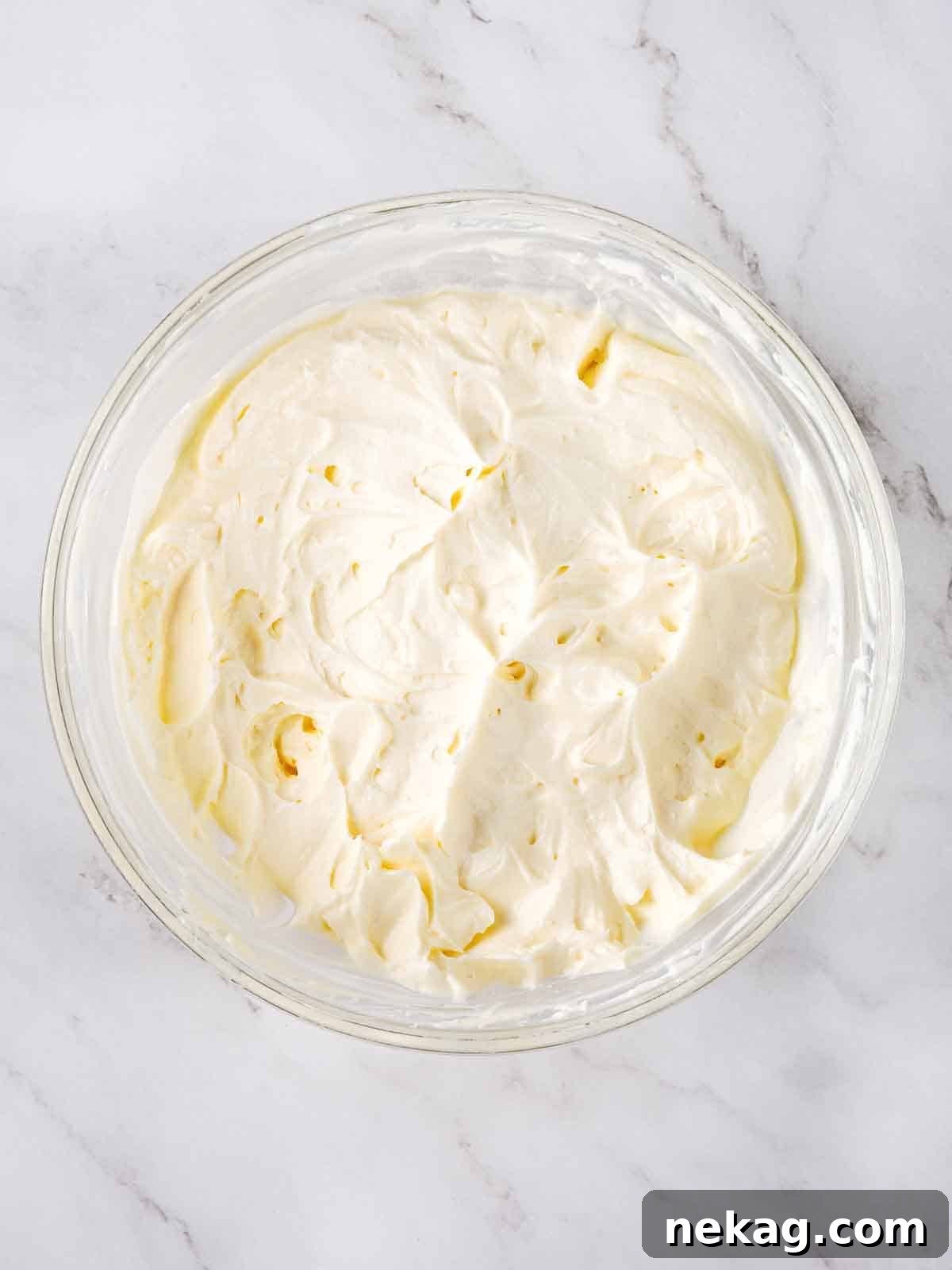 Fluffy cream cheese frosting in a clear bowl, ready to be used.
