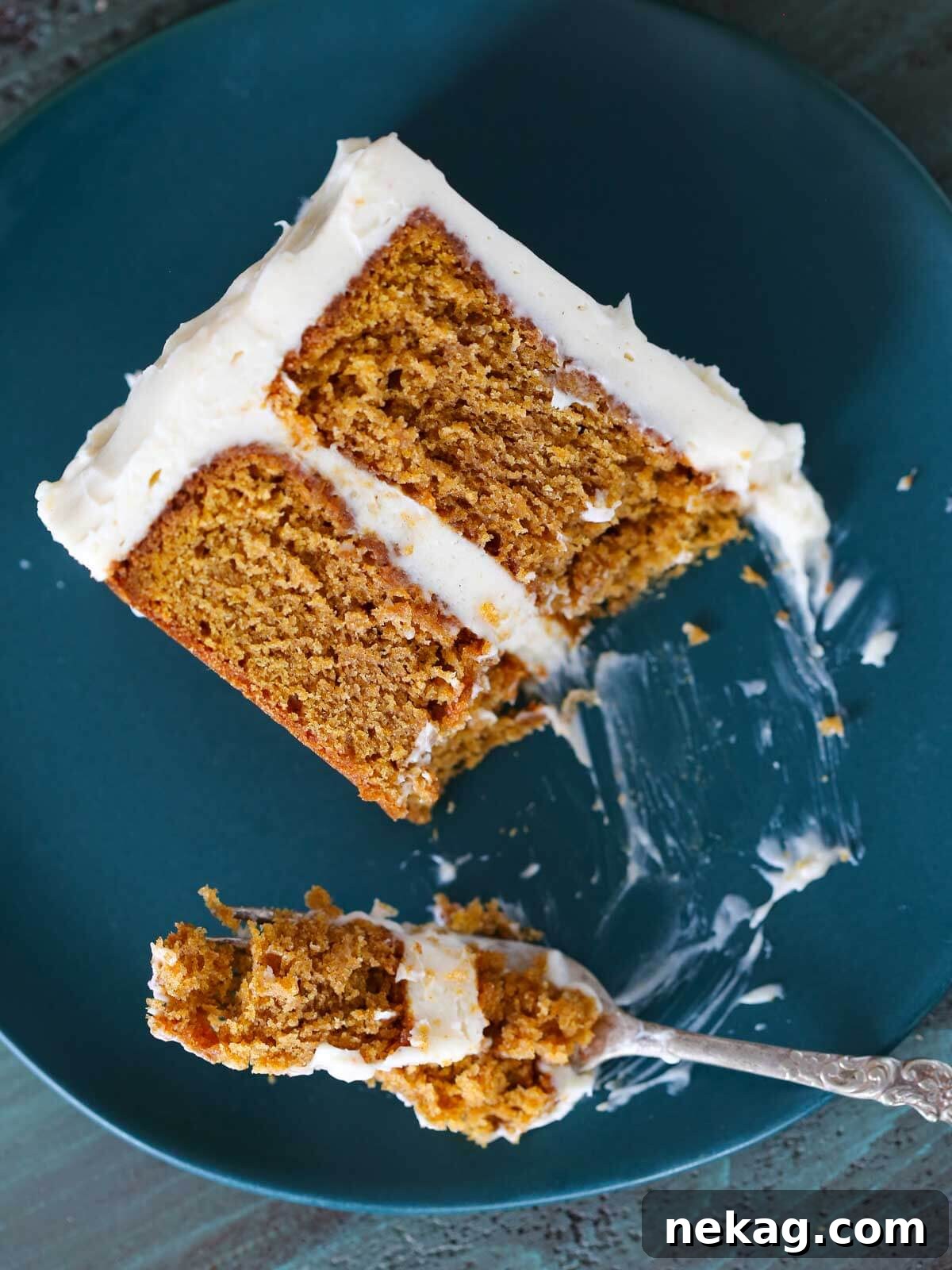 A fork filled with pumpkin cake from a plated slice, showing creamy frosting.
