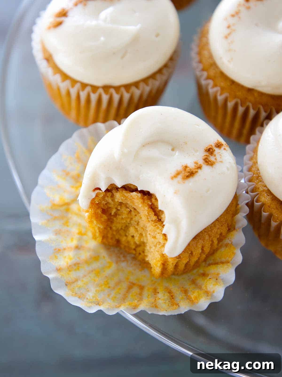 Spiced cream cheese buttercream on pumpkin cupcakes arranged on a cake stand.