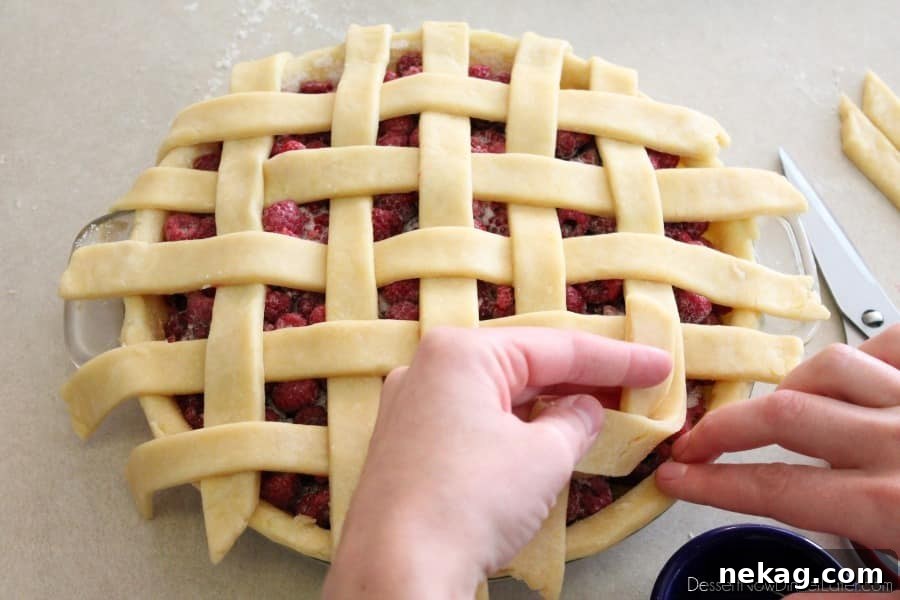 The edge of the bottom pie crust being moistened with water, preparing it to seal the lattice strips firmly in place.