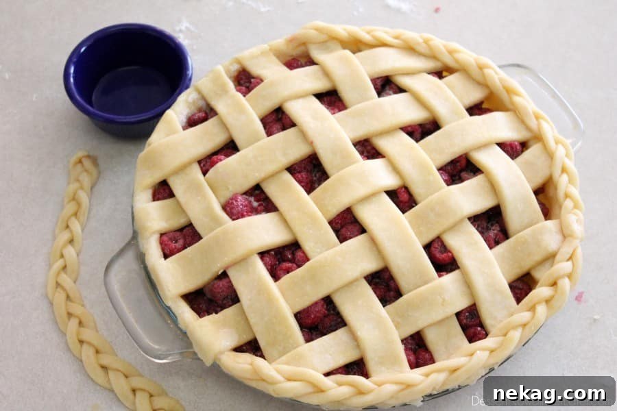 Braided pie crust being gently pressed onto the moistened edge of the pie, completing the decorative border.