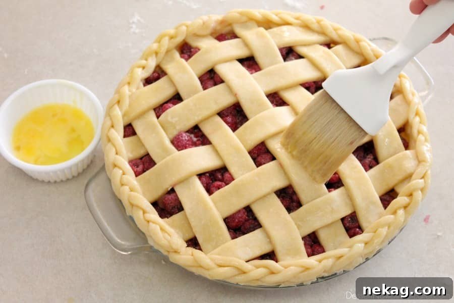 A whisked egg being gently brushed over the lattice pie crust and braided edge, preparing it for a golden bake.