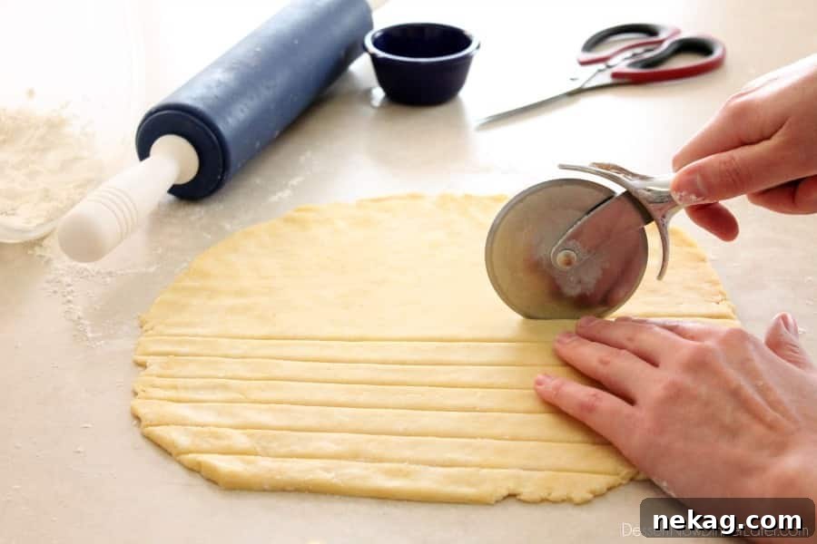 Multiple 1-inch wide pie crust strips neatly arranged on a flat surface, ready for the lattice weaving process.