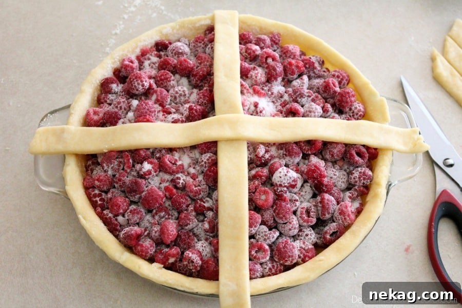 The initial step of forming a lattice crust, showing two pie crust strips criss-crossed over the center of a filled pie.