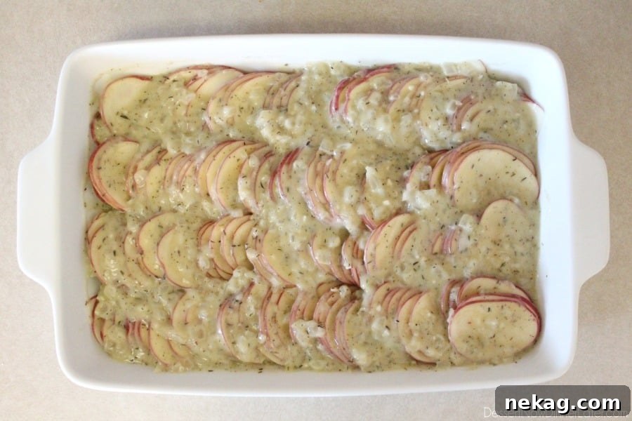 Pouring the creamy Tuscan sauce over layers of thinly sliced potatoes in a baking dish.