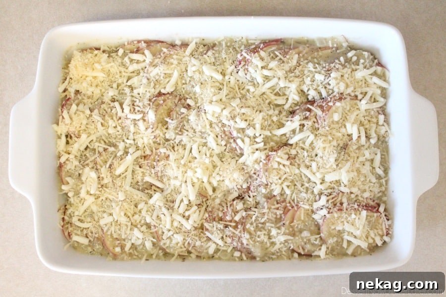 Tuscan Scalloped Potatoes topped with a generous sprinkle of shredded Parmesan and Mozzarella cheeses before baking.