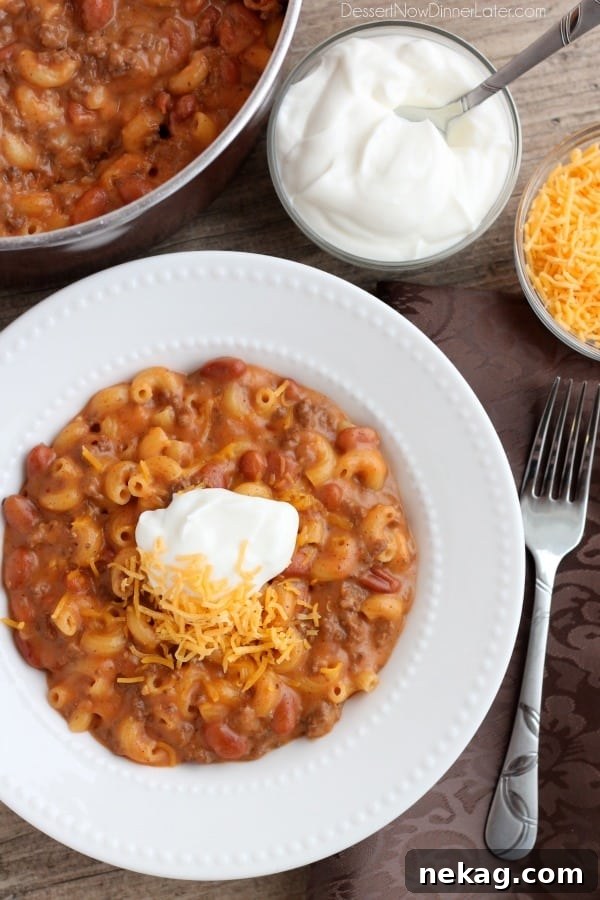 Close-up of a generously topped bowl of Chili Mac and Cheese with sour cream and shredded cheese, emphasizing its comforting appeal.