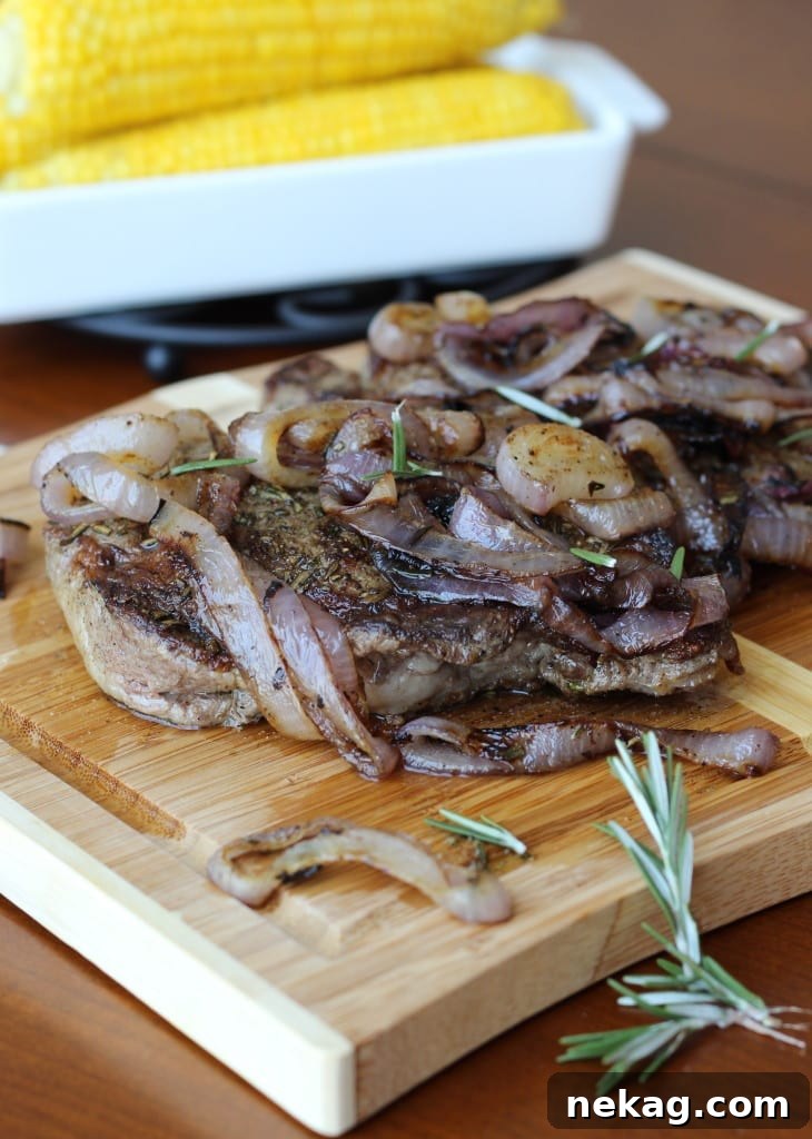 A delicious serving of Rosemary Rubbed Rib-Eye steak presented alongside beautifully charred red onions on a white plate.