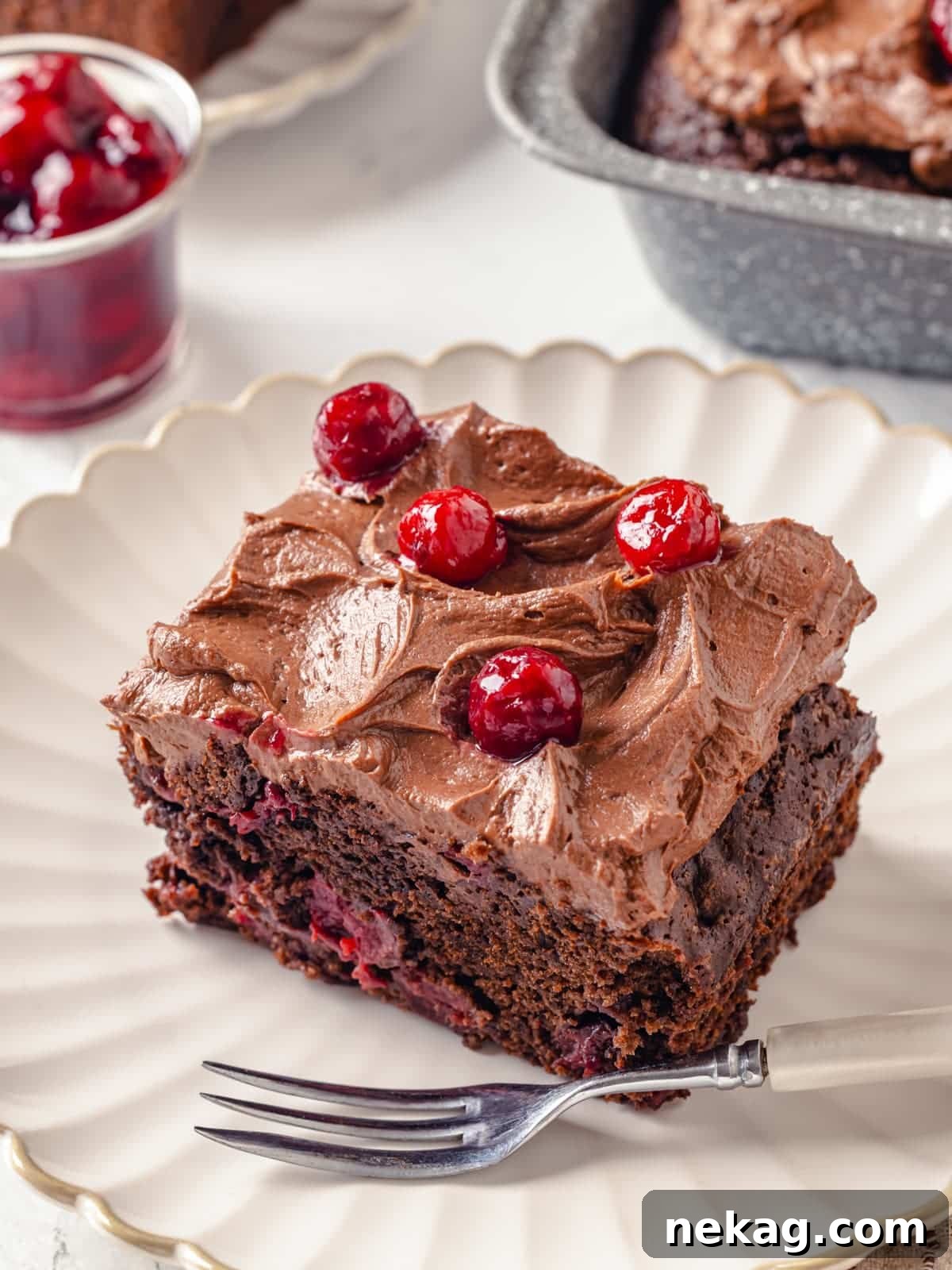 A rich chocolate cake, perfectly topped with swirled cream cheese frosting and adorned with fresh cherries, presented on a decorative plate.