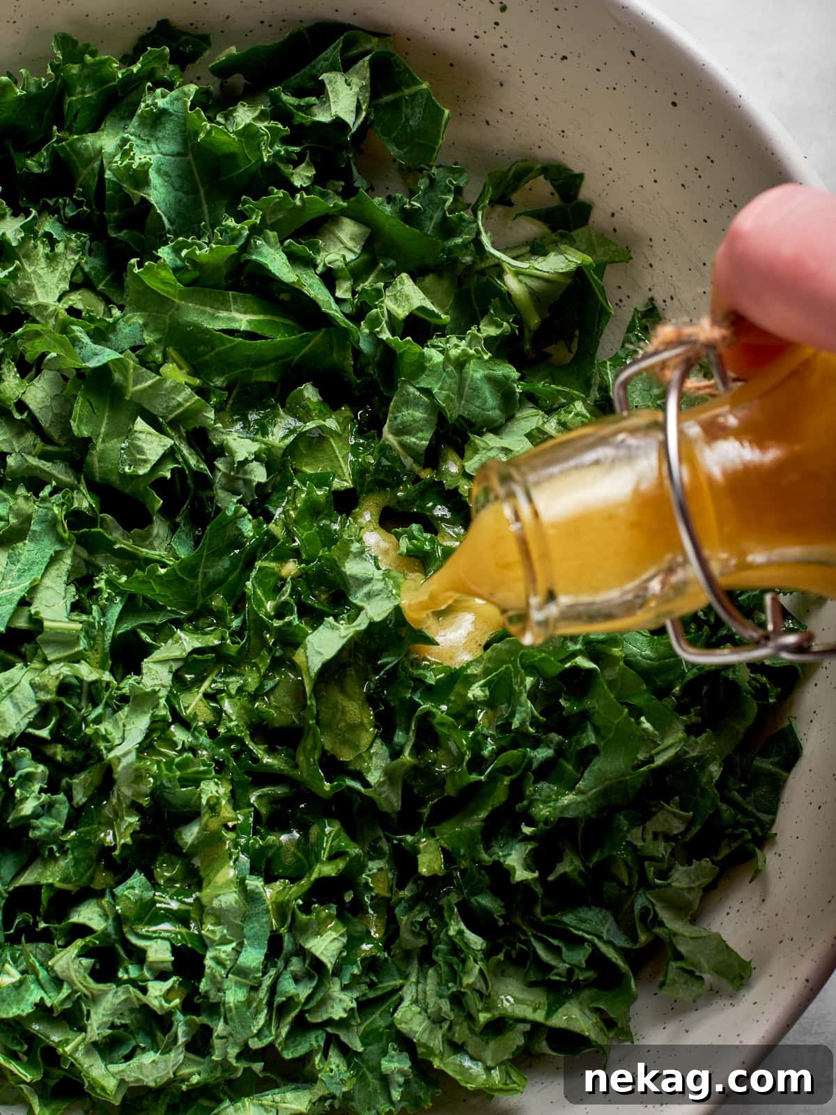 Champagne vinaigrette generously poured over fresh kale salad greens in a large serving bowl, ready to enjoy.