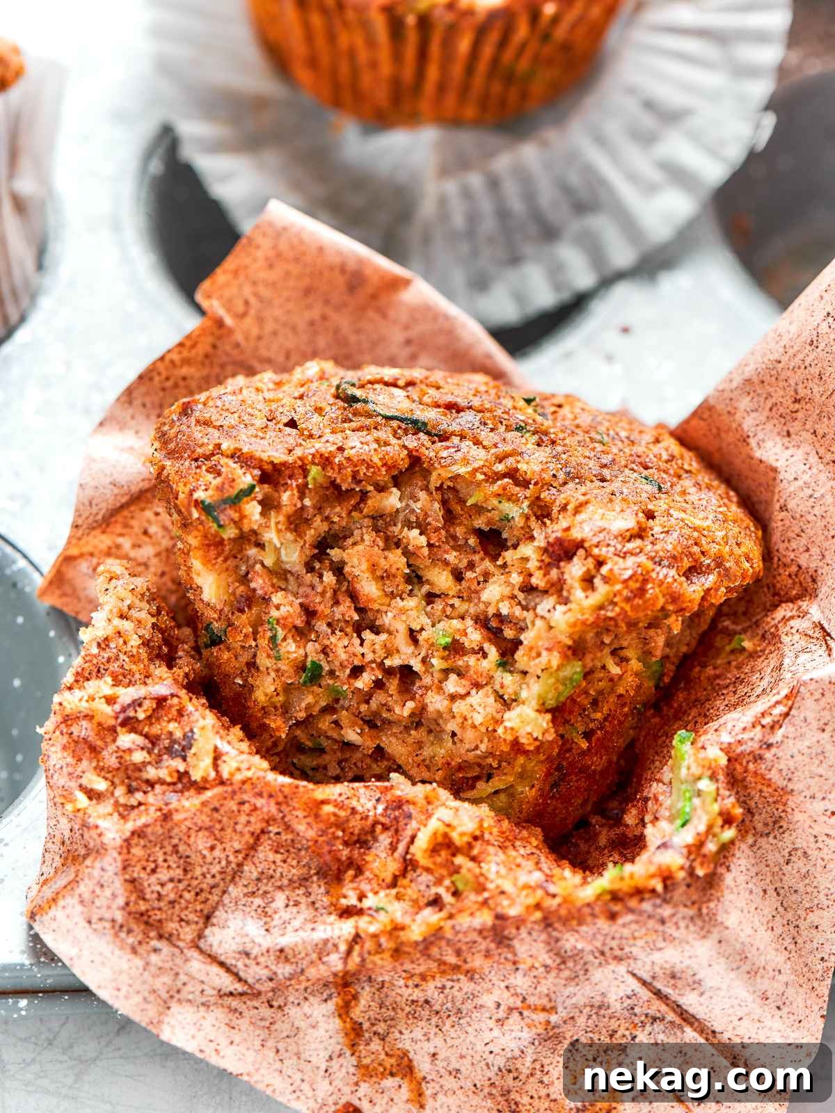 Zucchini muffin split open revealing soft tender crumb and flecks of zucchini.