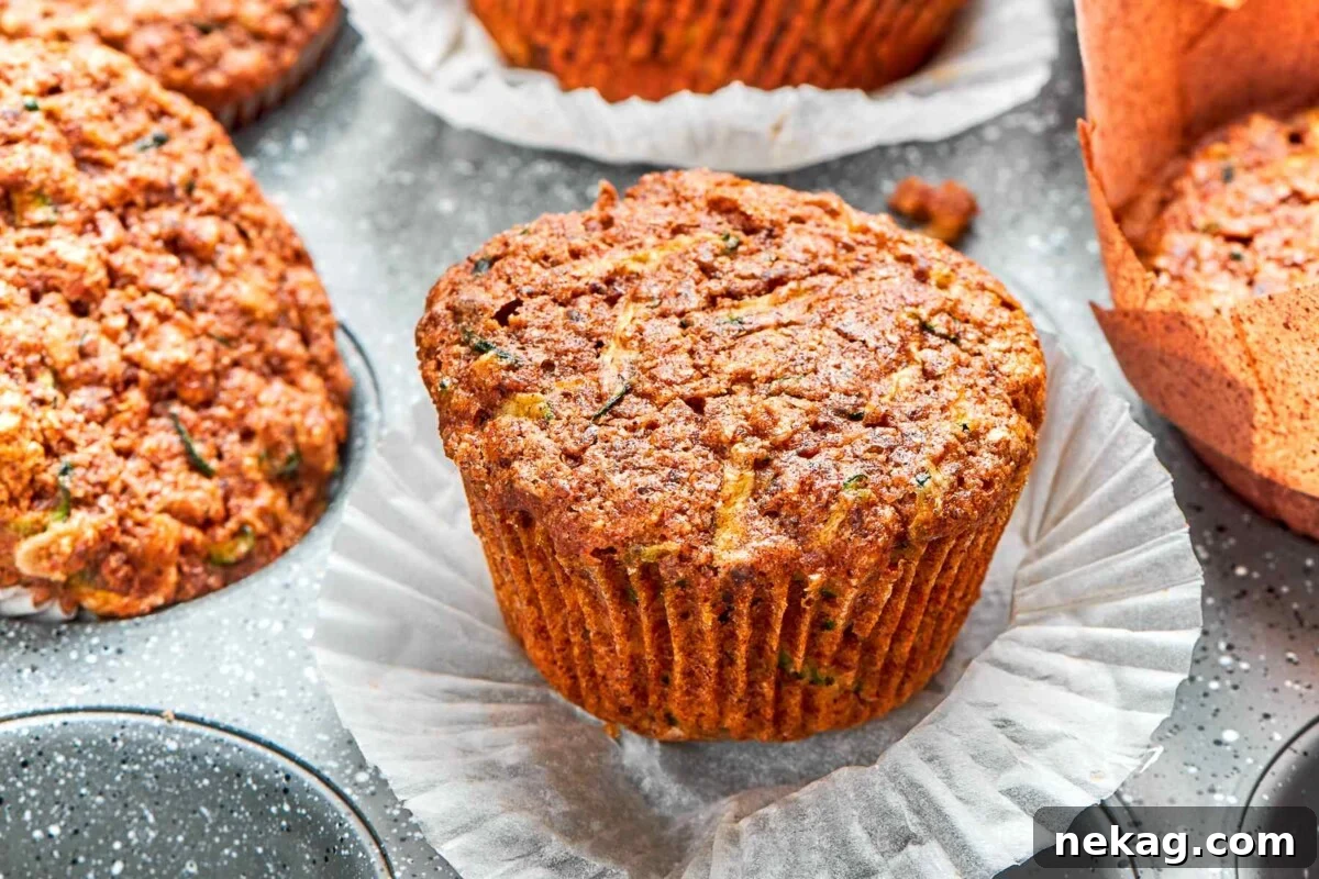 Zucchini muffin with wrapper peeled down revealing moist crumb and flecks of zucchini.