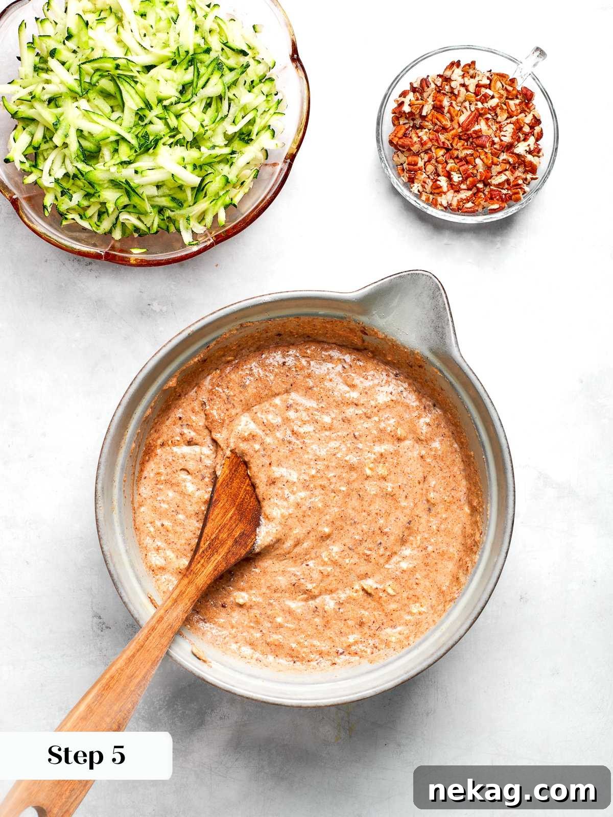 Mixing wet and dry ingredients together to form zucchini muffin batter.
