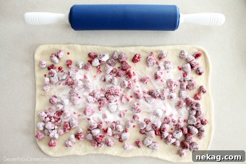 Dough rolled into a rectangle with sugar coated raspberries on top.