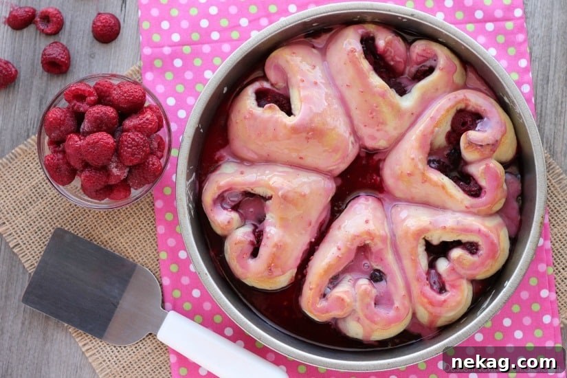 Glazed heart shaped rolls in pan with raspberries.