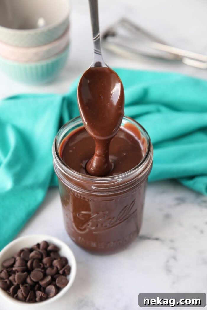 Homemade hot fudge recipe in a mason jar being drizzled with a spoon.