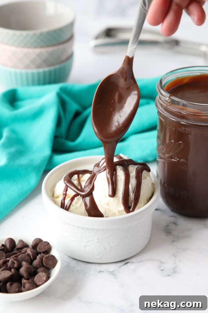 Hot fudge sauce being drizzled over vanilla ice cream with a spoon.