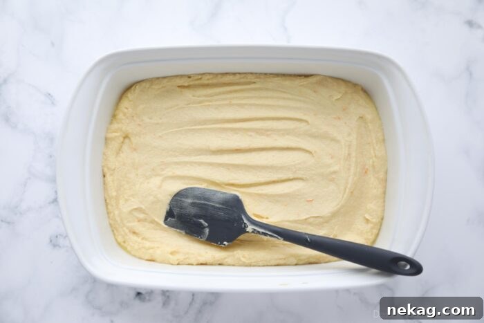 Spreading orange brownie batter into a 13x9-inch pan with a spatula.