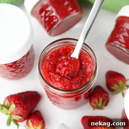Low-Sugar Strawberry Freezer Jam Recipe with Video Tutorial 13 Top view of an open jar of low-sugar strawberry jam with a spoon inside.