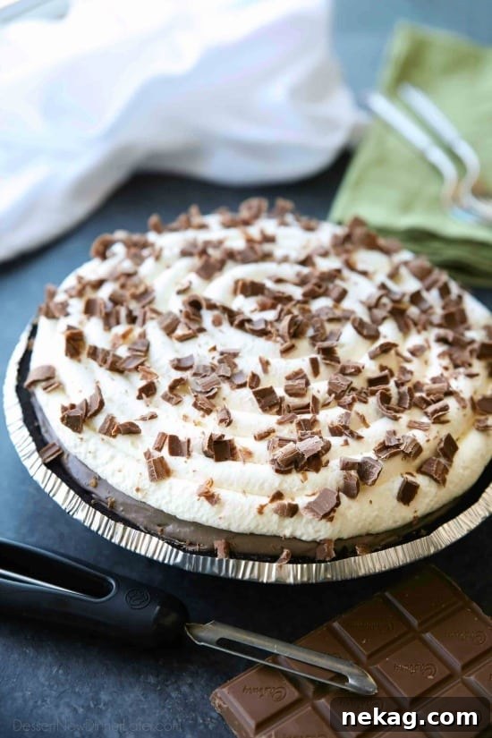 Close-up of a no-bake cheesecake slice showing distinct vanilla and chocolate layers with whipped cream and chocolate shavings.