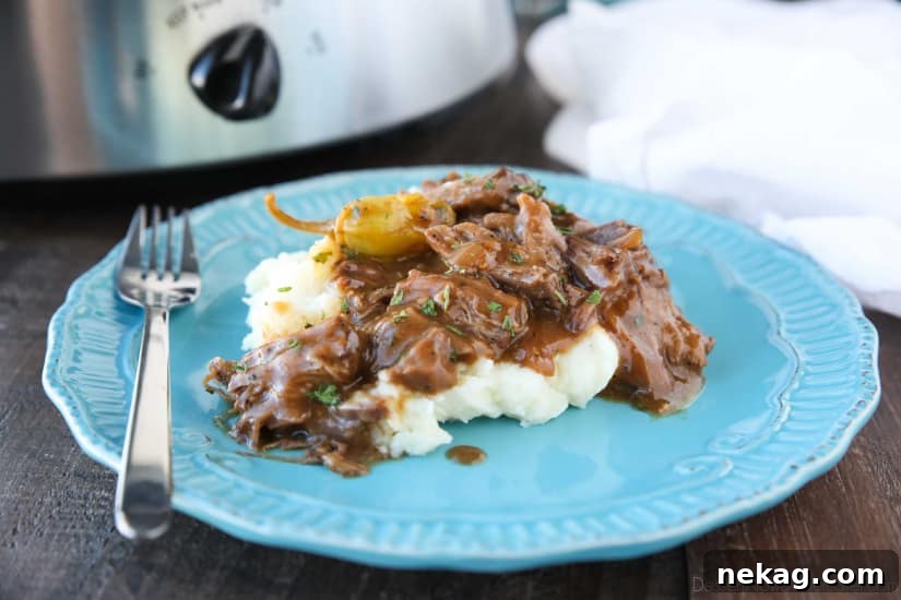 Plate of mashed potatoes topped with Mississippi Pot Roast shredded beef in gravy.