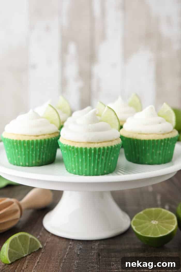 Key Lime Cupcakes sitting on a cake stand with lime wedges in frosting.