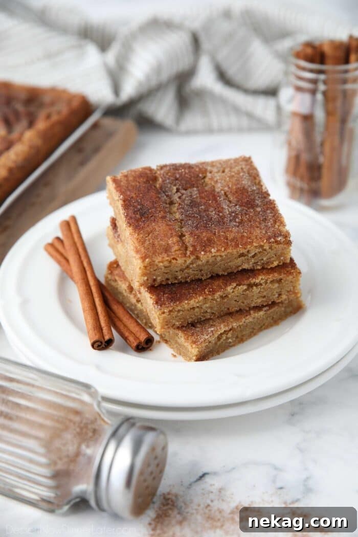 Chewy Cinnamon Bars with Brown Sugar Glaze 2 Stack of cinnamon bars on a plate with extra cinnamon-sugar on top and cinnamon sticks on the side.