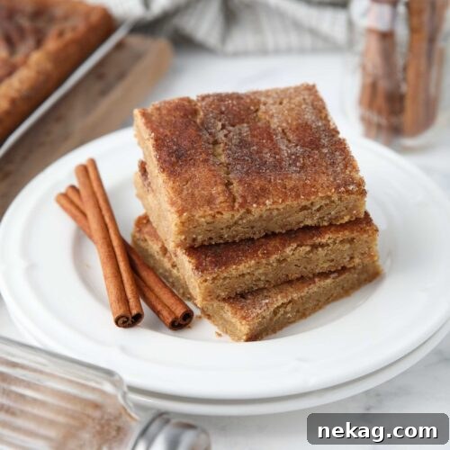 Chewy Cinnamon Bars with Brown Sugar Glaze 11 Stack of cinnamon bars on a plate with extra cinnamon-sugar on top and cinnamon sticks on the side.