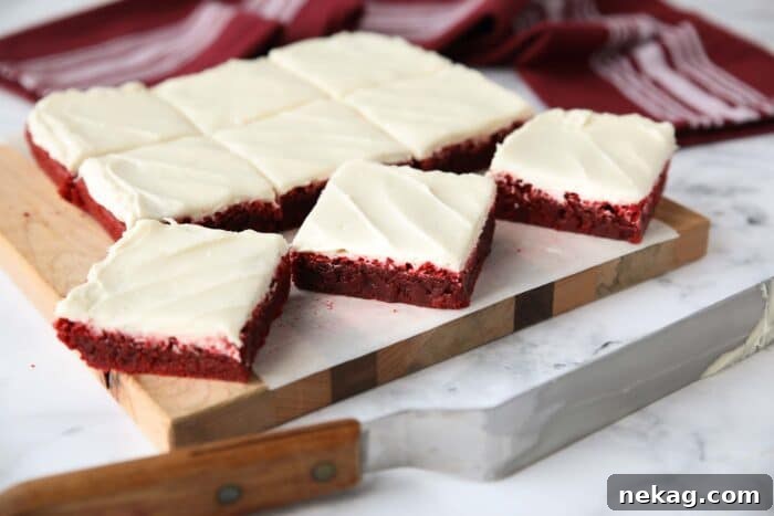 Decadent Red Velvet Brownie Recipe with Cream Cheese Swirl 11 Square pan of Red Velvet Brownies with cream cheese frosting cut into squares on a cutting board.
