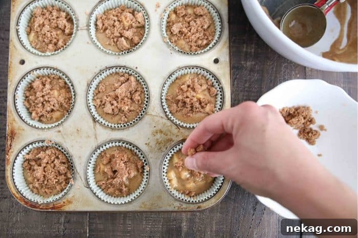 Homemade Apple Cinnamon Muffins Recipe for Fall Baking 7 Sprinkling the crumb topping on the apple cinnamon batter filled muffin cups.