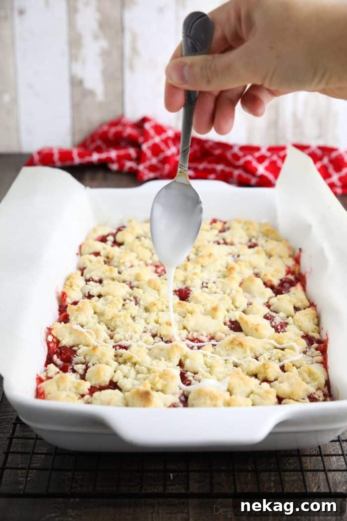 Glaze being drizzled over the top of cherry crumb bars with a spoon.