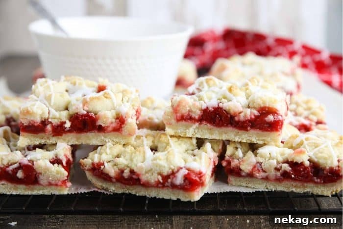 Cherry Pie Bars stacked on top of each other with a bowl of glaze in the background.