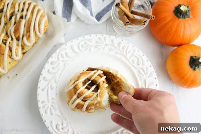 Pumpkin Spice Cinnamon Rolls with Cream Cheese Glaze 4 A hand peeling apart the outer layer of the pumpkin cinnamon roll.