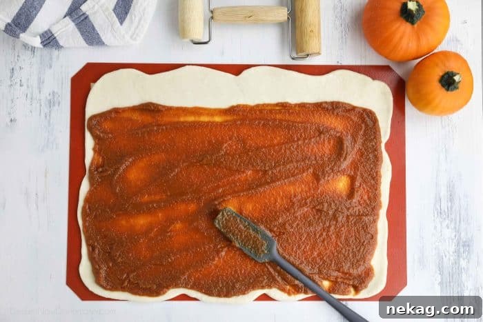 Pumpkin Spice Cinnamon Rolls with Cream Cheese Glaze 7 Pumpkin filling being spread on top of rolled out dough.