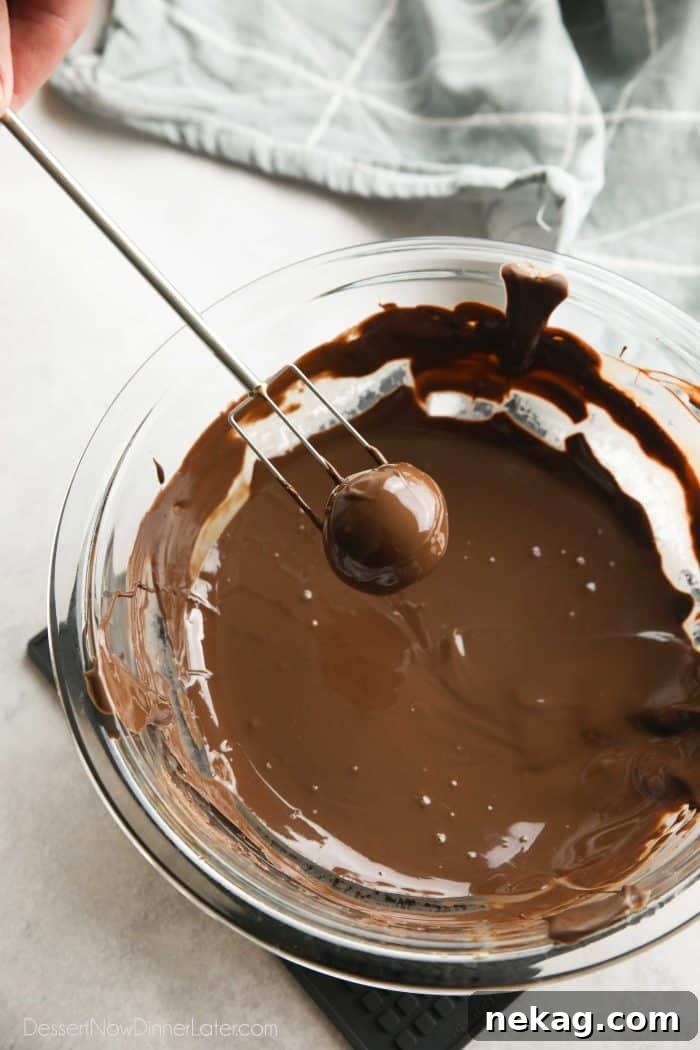 Using a chocolate dipping fork to coat a peanut butter ball in melted chocolate.