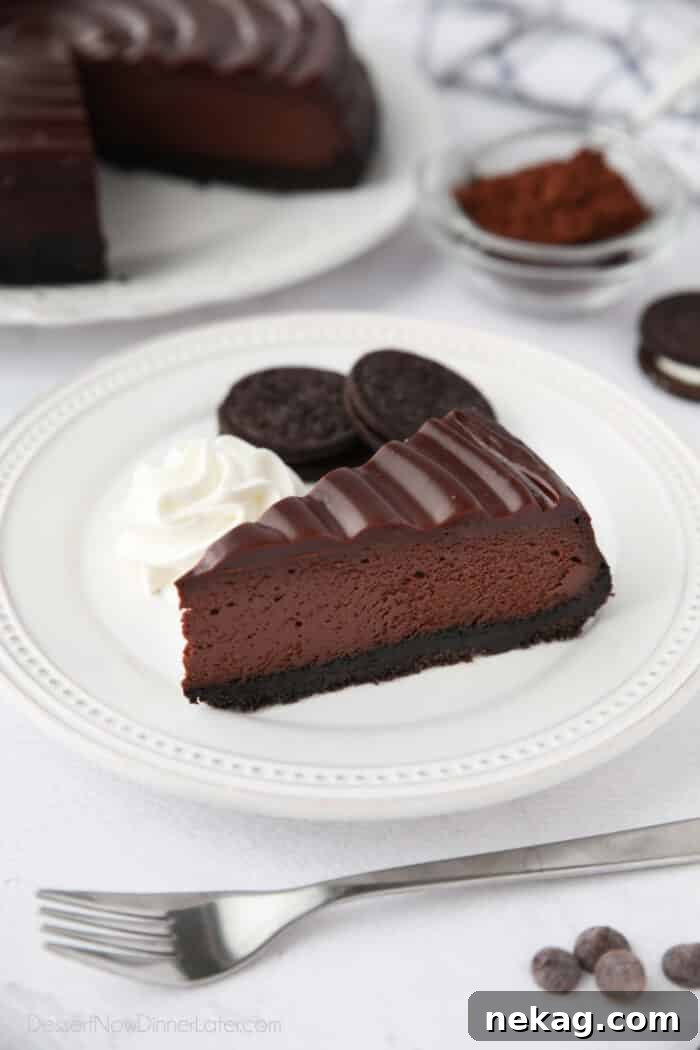 A slice of Triple Chocolate Cheesecake on a plate with Oreos and whipped cream on the side.