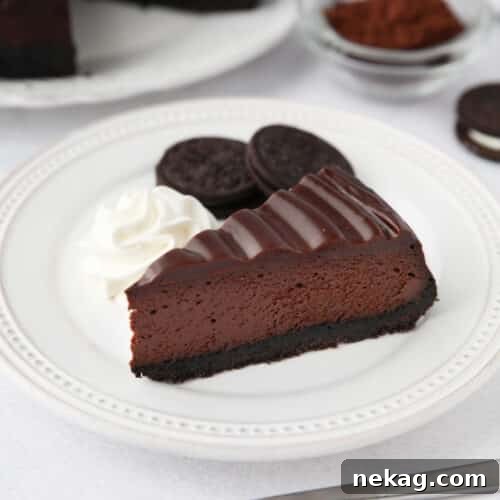 A slice of Triple Chocolate Cheesecake on a plate with Oreos and whipped cream on the side.
