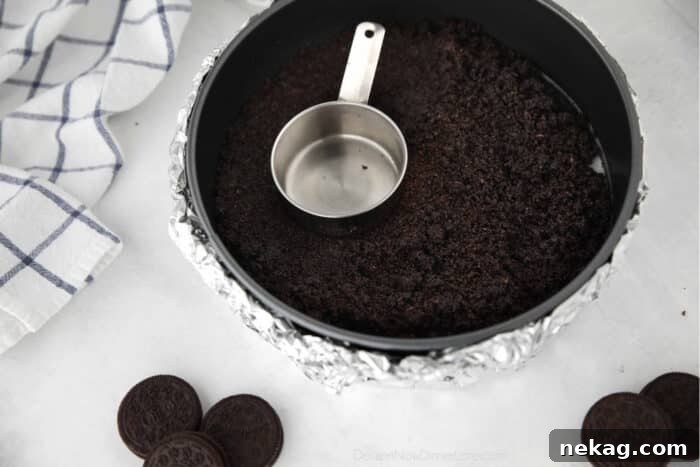Oreo crust being pressed into a springform pan for chocolate cheesecake.