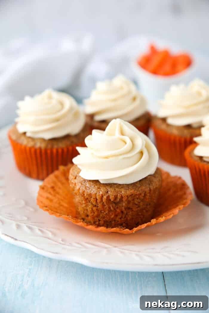 Moist Carrot Cake Cupcakes with Step-by-Step Video Tutorial 2 Carrot Cake Cupcakes on a plate. Focus is on a cupcake with the paper liner pulled down on the sides to show velvety texture of cake.