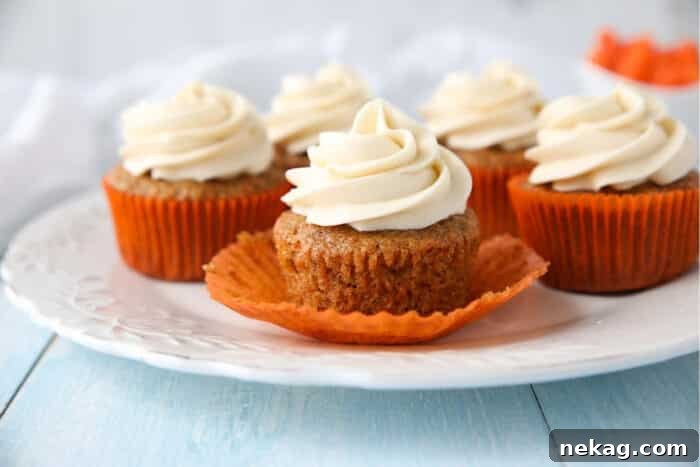 Moist Carrot Cake Cupcakes with Step-by-Step Video Tutorial 4 Carrot Cake Cupcakes on a plate. Focus is on a cupcake with the paper liner pulled down on the sides.