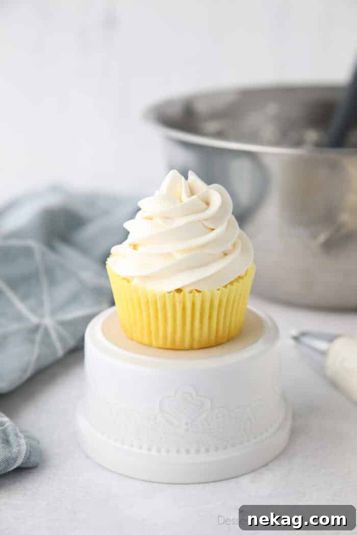 Whipped Cream Cheese Frosting Recipe (Video Tutorial) 2 Focus is on a cupcake piled high with whipped cream cheese frosting.