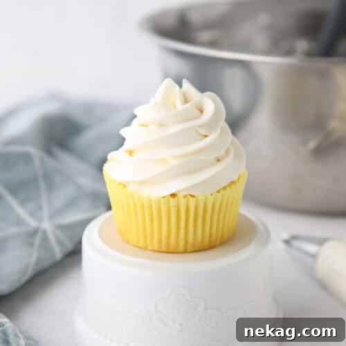 Whipped Cream Cheese Frosting Recipe (Video Tutorial) 13 Focus is on a cupcake piled high with whipped cream cheese frosting.